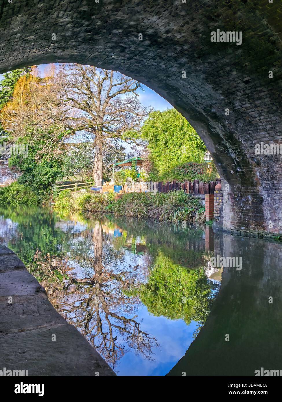 Perfect circular reflection of autumn trees and canal bridge seen through a historic stone arch on the Stroudwater Canal, Stroud, Cotswolds, - Smartphone Captured Stock Image