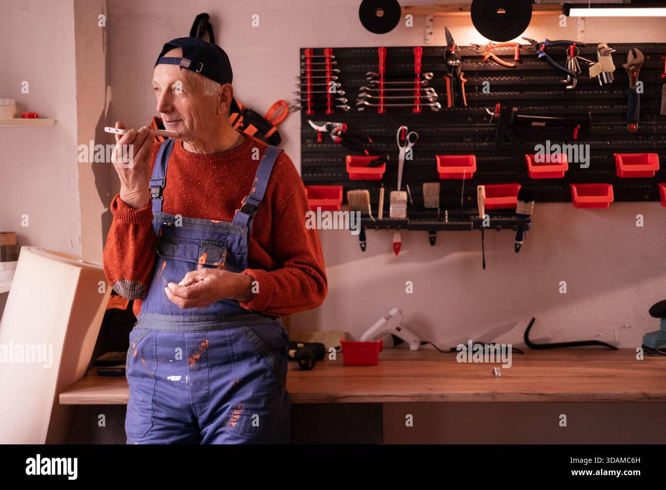 Senior Elderly Mechanic sending voice note or message using smartphone mic in workshop. copy space Stock Photo