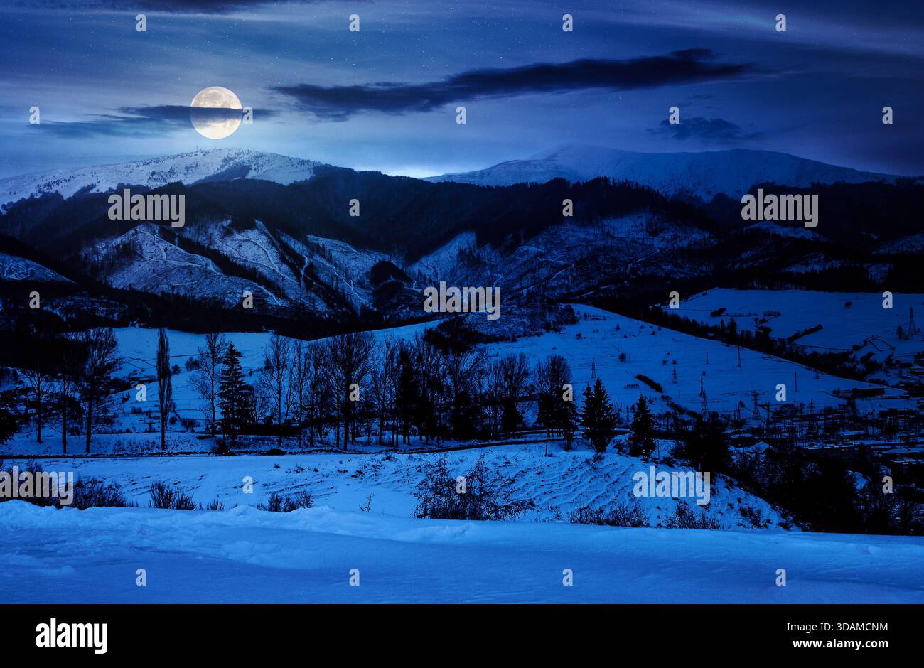winter sky over the mountains at night. beautiful light on snowy tops of ridge in full moon light. rural landscape with serpentine pass in to valley. Stock Photo