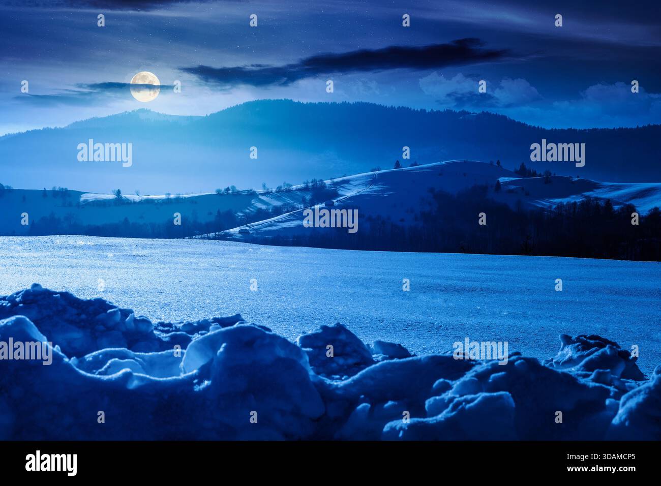 beautiful winter landscape with snow covered rolling hills under dark sky at night. majestic mountains in full moon light. frosty countryside scenery. Stock Photo