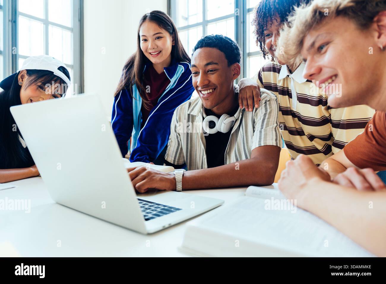 Multiethnic group of young students meeting at the library - group of diverse young students collaborating on laptop, smiling and studying together in Stock Photo