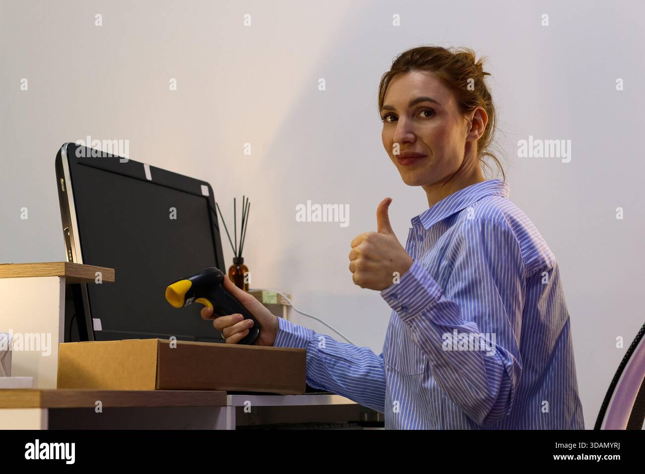 Staff in logistics point thumbs up while directing scanner toward box on work surface. Stock Photo