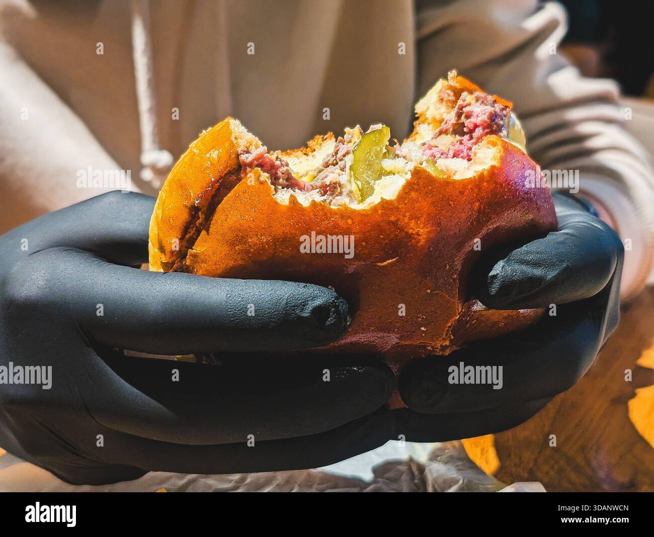 hands in black gloves holding half eaten gourmet beef burger Stock Photo