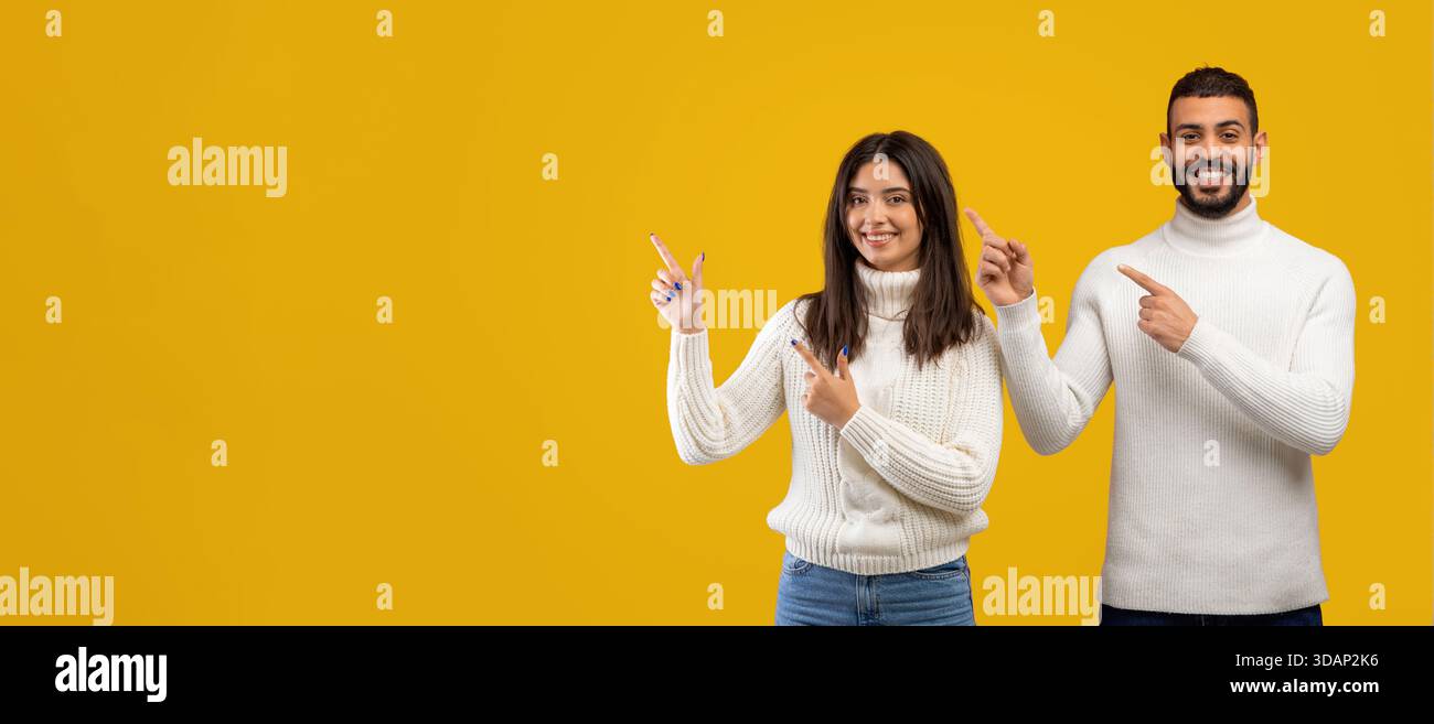 Two People Smiling and Pointing at Something on a Bright Yellow Background Stock Photo