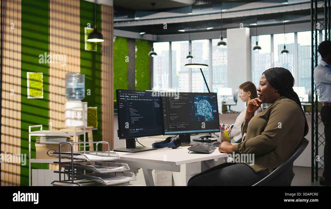 Jolly female programmer at office desk pleased after developing application using machine learning automation. Joyous employee satisfied after debugging applications using neural networks, camera A Stock Photo