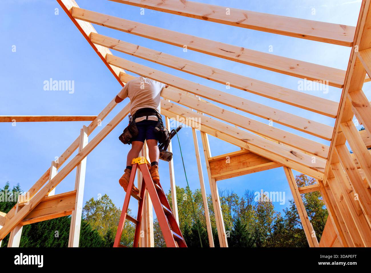 Worker constructs wooden roof beams frame while standing on ladder at ...