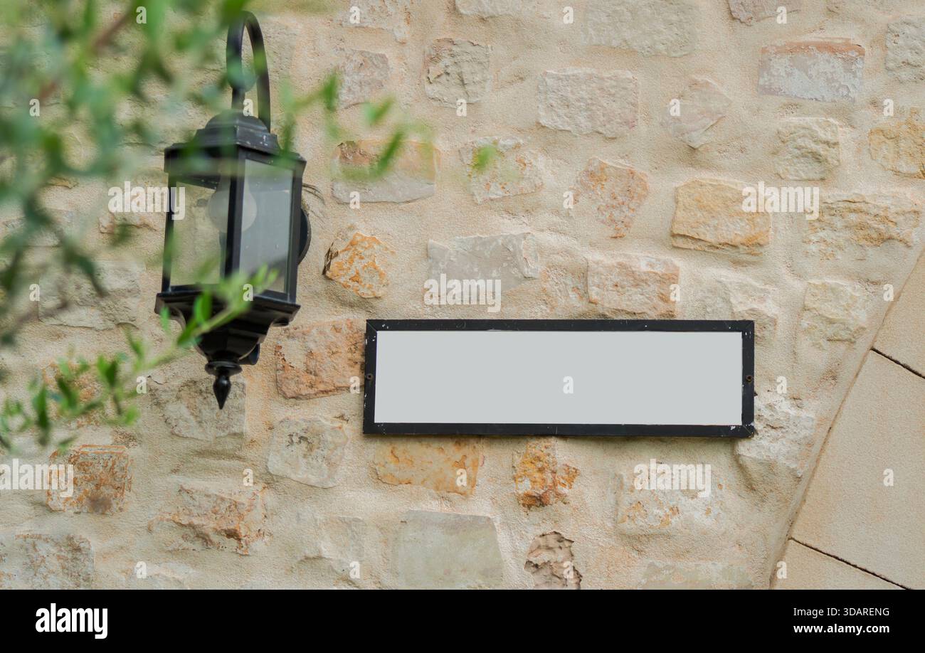 Selective focus of beige brick wall with white empty billboard for writing nearby is an old lamp hanging on the wall. Stock Photo
