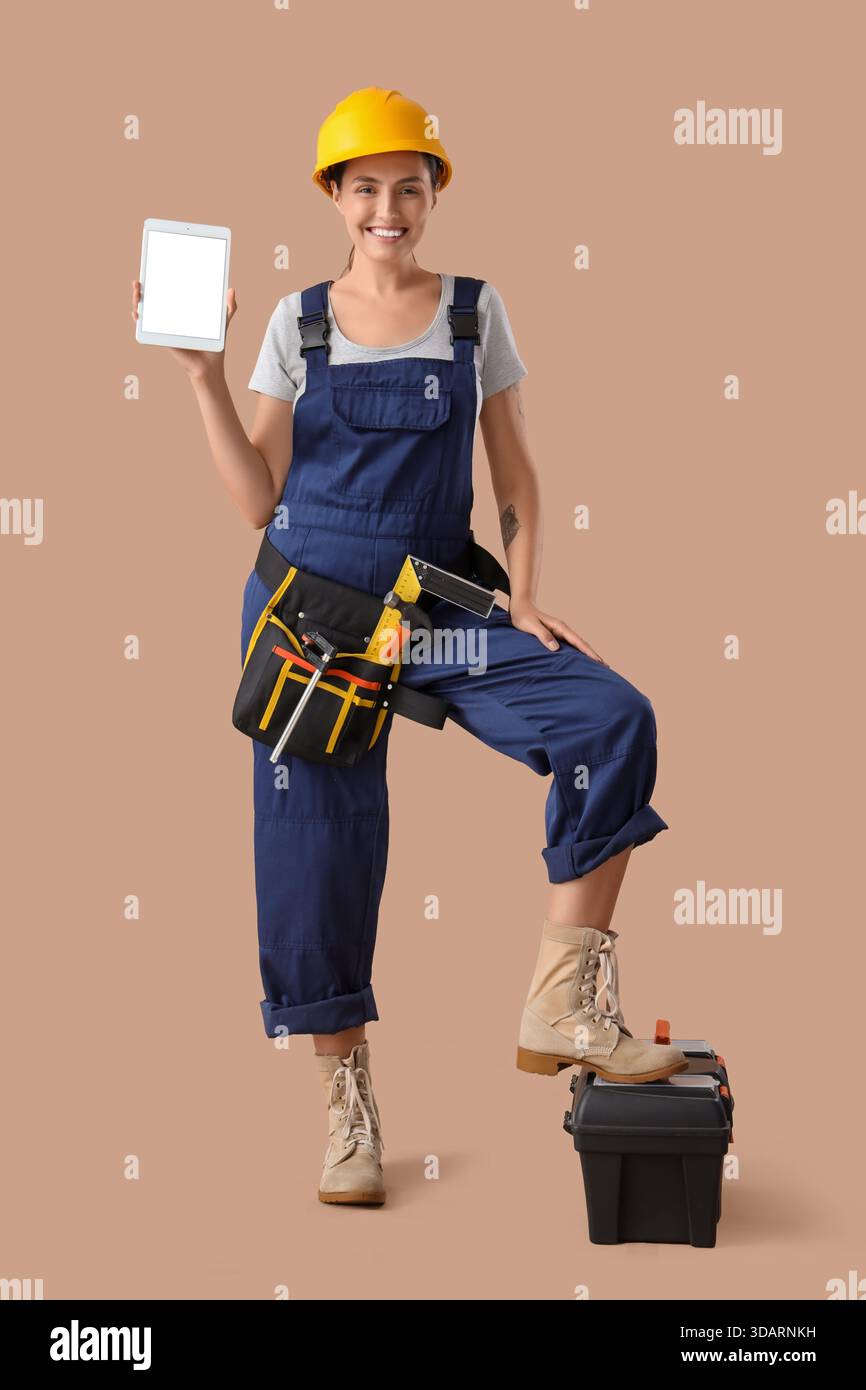 Female builder with blank tablet computer and tools on beige background Stock Photo