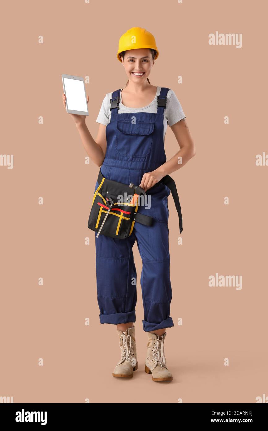 Female builder with blank tablet computer on beige background Stock Photo