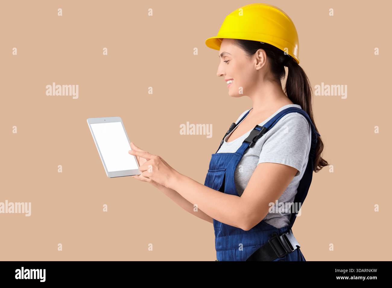 Female builder with blank tablet computer on beige background Stock Photo