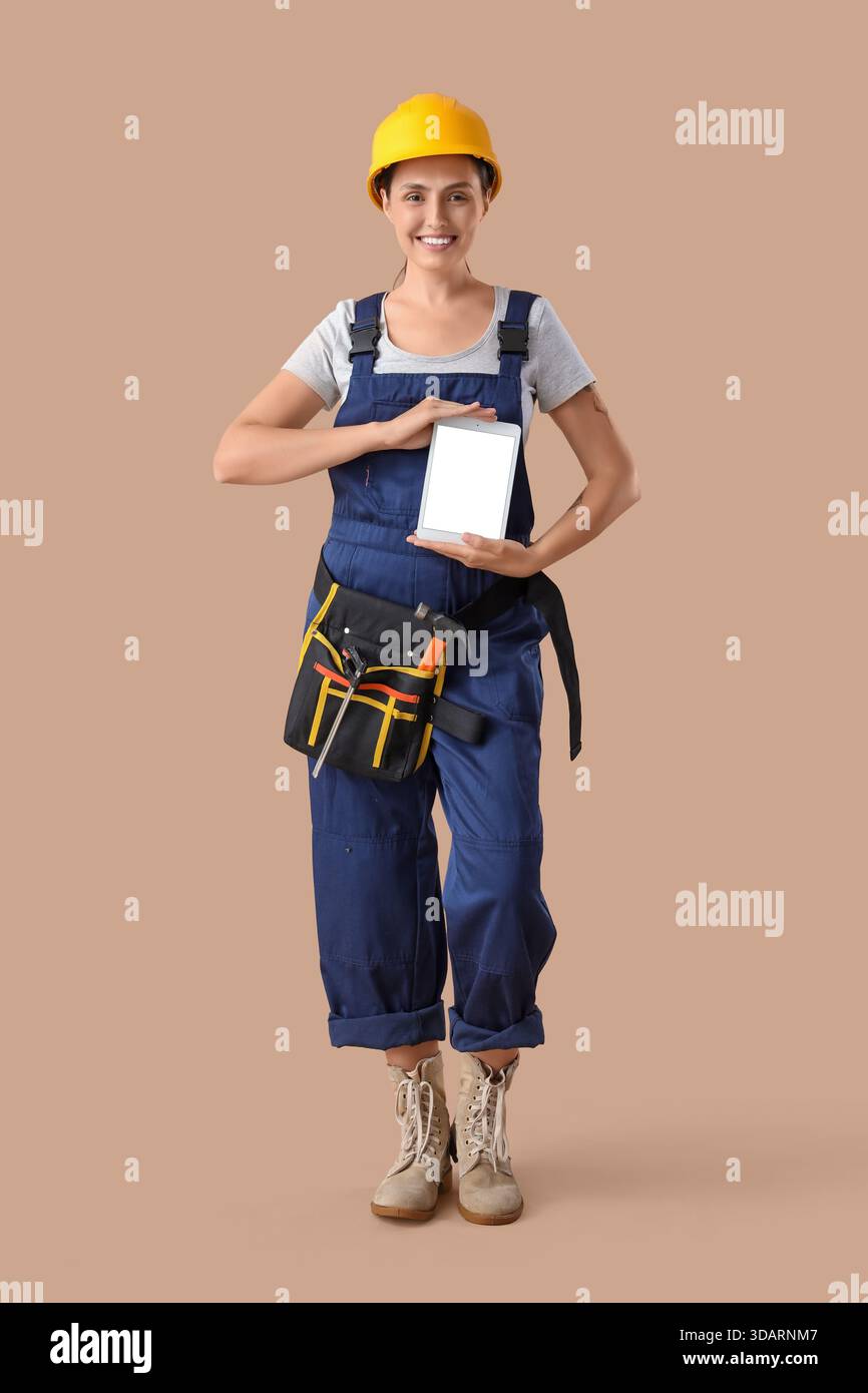 Female builder with blank tablet computer on beige background Stock Photo
