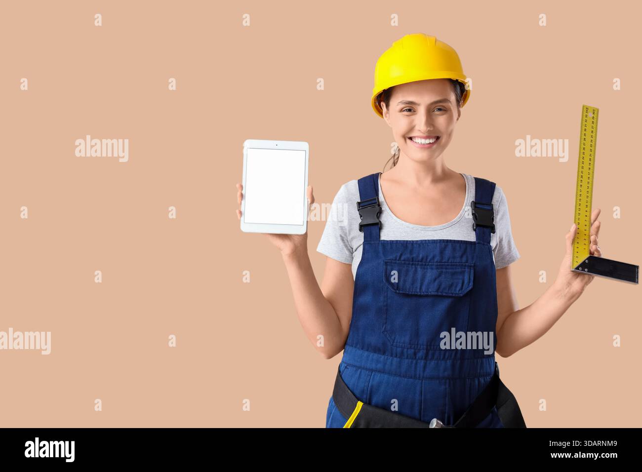 Female builder with blank tablet computer and ruler on beige background Stock Photo
