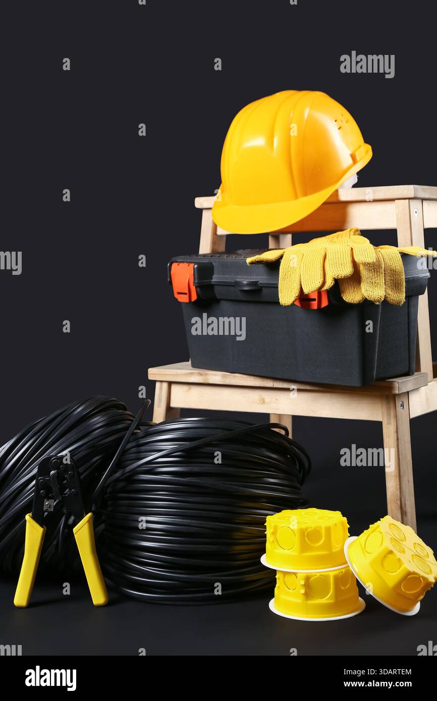 Stepladder with electrician tools, rolled cables and hardhat on black background Stock Photo
