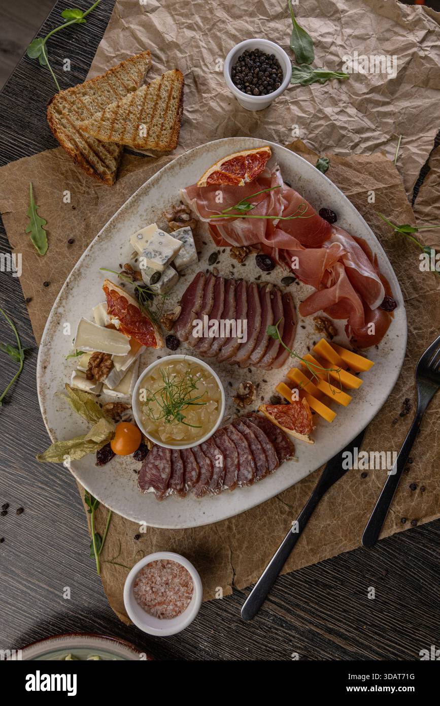 Cold plate featuring assorted cheeses, cold cuts, and appetizers on rustic table Stock Photo