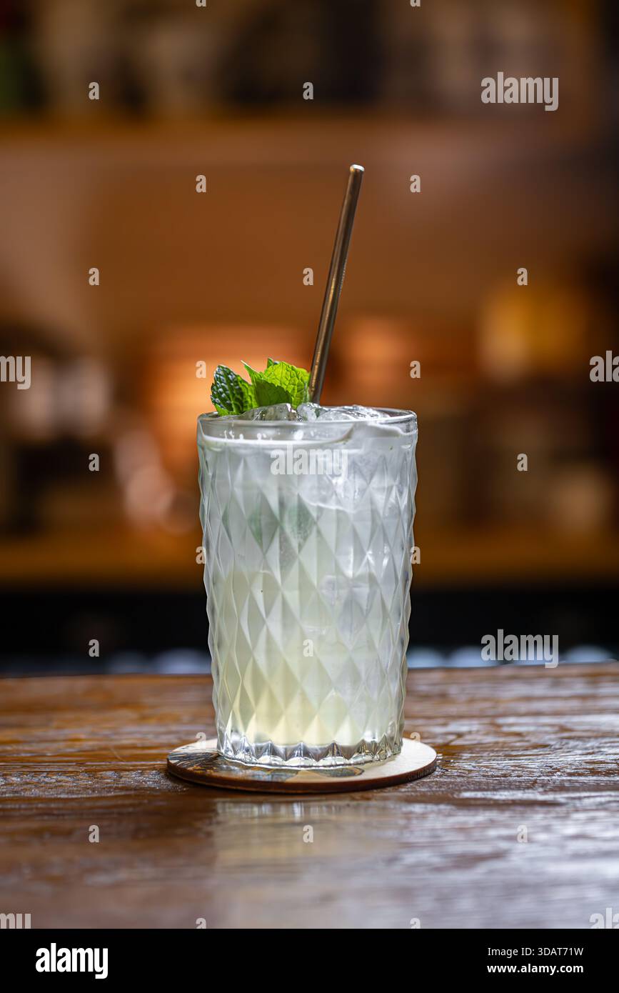 Refreshing lemon cocktail with ice decorated with mint leaf on a rustic wooden bar counter Stock Photo