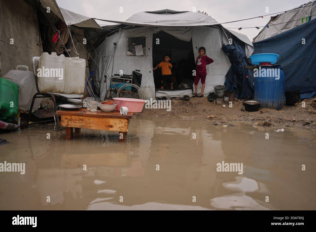 Children stand at the entrance of their family's tent next to a flooded ...