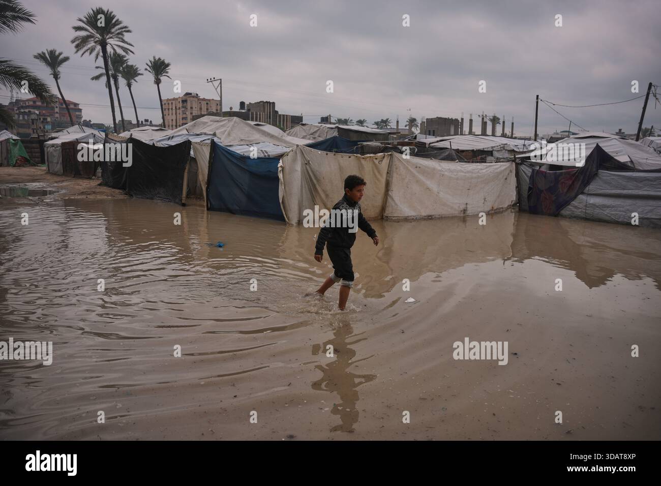 A Palestinian youth walks through a flooded area in a temporary tent ...