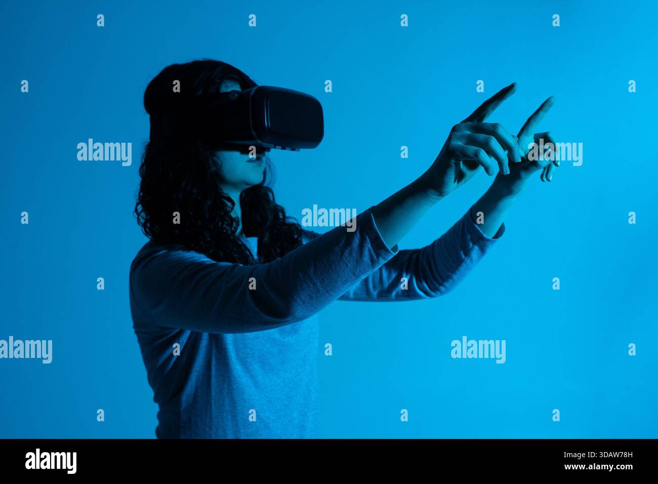 A woman interacts with a virtual interface, reaching outward with both hands while wearing a VR headset Stock Photo