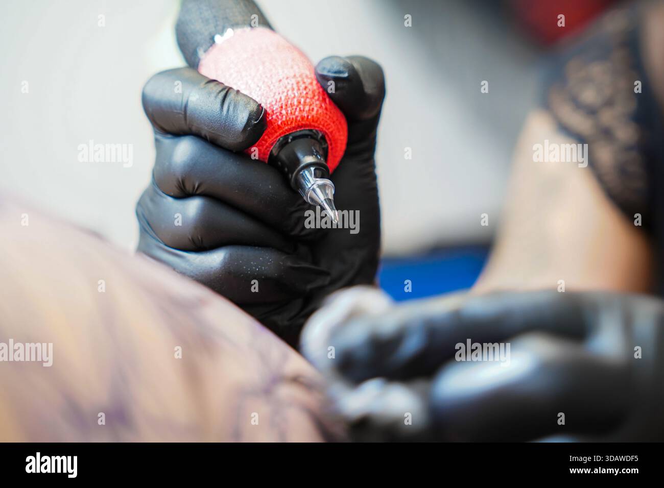 A female tattoo artist works diligently in a tattoo studio, focusing on creating intricate designs on a client’s skin, showcasing skill and precision Stock Photo