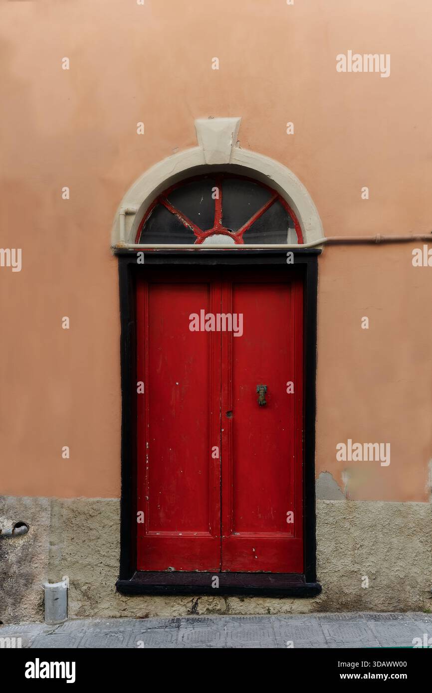 Red wooden door set in an old plastered wall, Italy Stock Photo