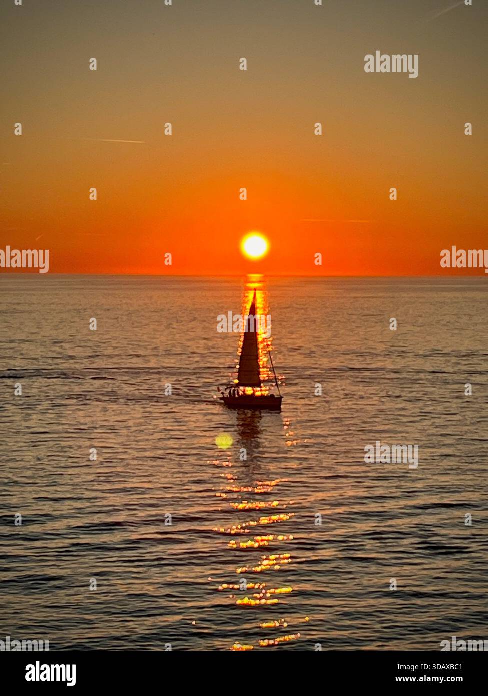 A lone sailboat gliding through molten gold as the sun sinks into the Adriatic - Smartphone Captured Stock Image