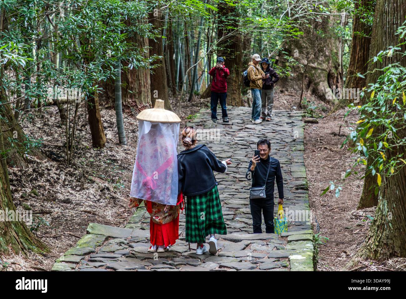 Dressed in kimonos like in the Heian period, tourists become an attraction for other tourists here on Daimon-zaka near Kumano Nachi Taisha. Tourists photograph a person dressed in traditional Japanese clothing on the rocky Kumano Kodo pilgrimage route in Nachikatsuura. Wakayama Prefecture, Japan Stock Photo