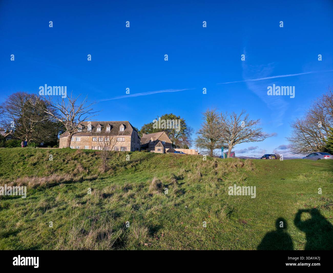 Classic Cotswolds Stone Farmhouse on Grassy Hill under Blue Sky - Smartphone Captured Stock Image