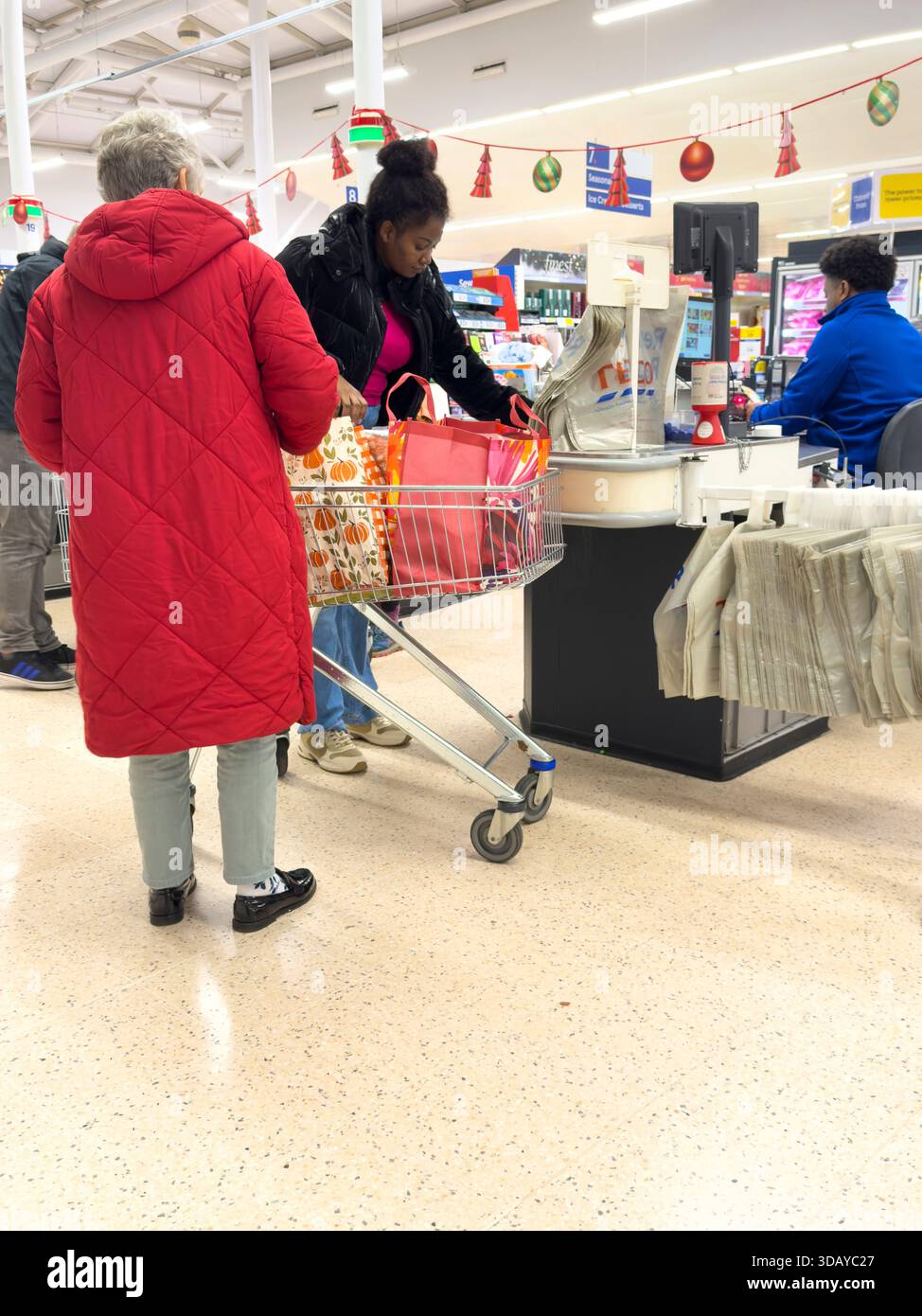 Winchester Hampshire England UK. 08.12.2025.  Customers  with Christmas shopping paying  at checkout desk in a local supermarket. - Stock Image