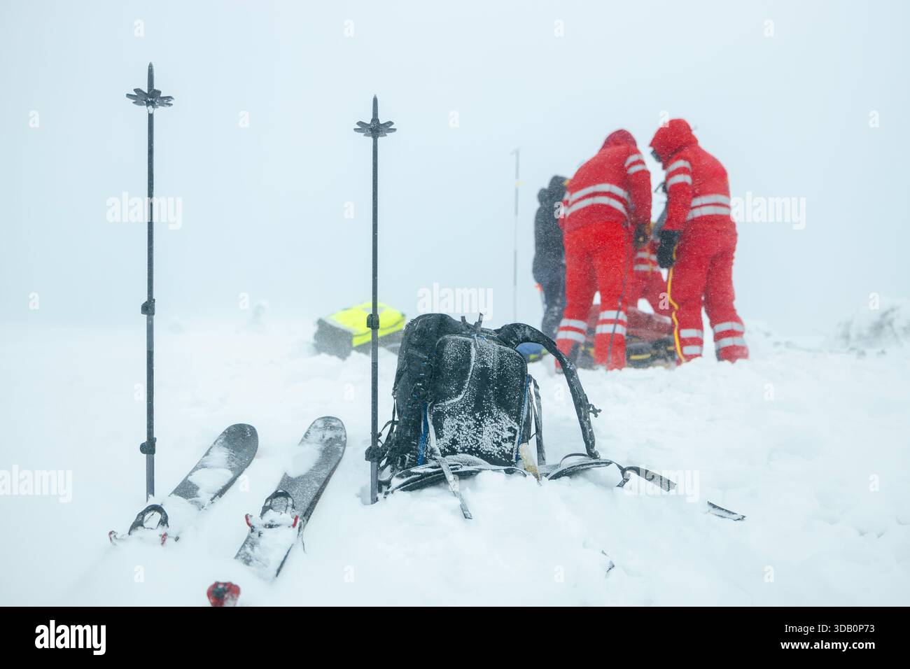Paramedic team of emergency service helping in mountains in winter during blizzard. Selective focus on ski poles in snow and backpack. Themes rescue i Stock Photo