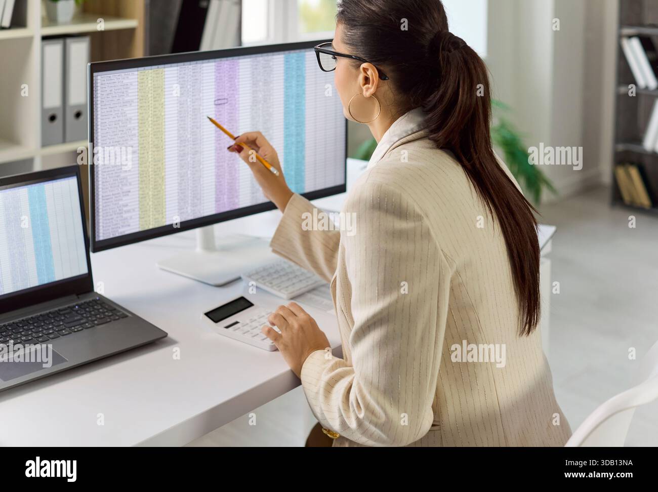 Businesswoman auditing data on large spreadsheet screen while working at desk Stock Photo