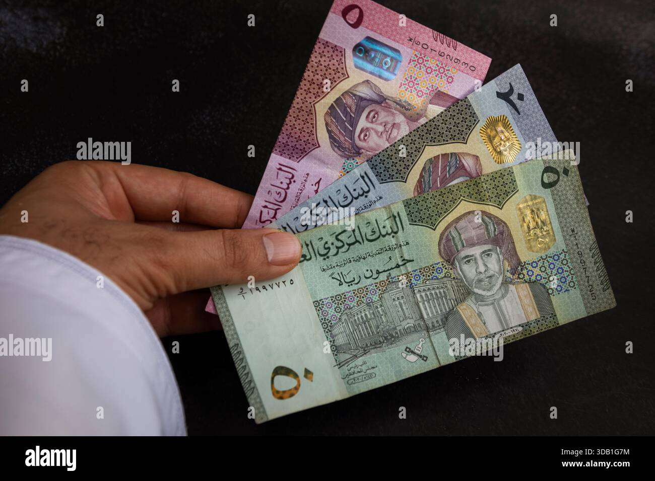 Hand holding Omani rial banknotes of different denominations, showing ...