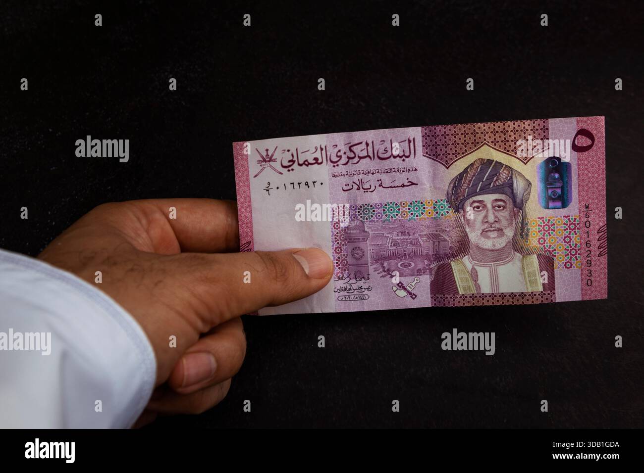 Hand holding Omani rial banknotes of different denominations, showing ...