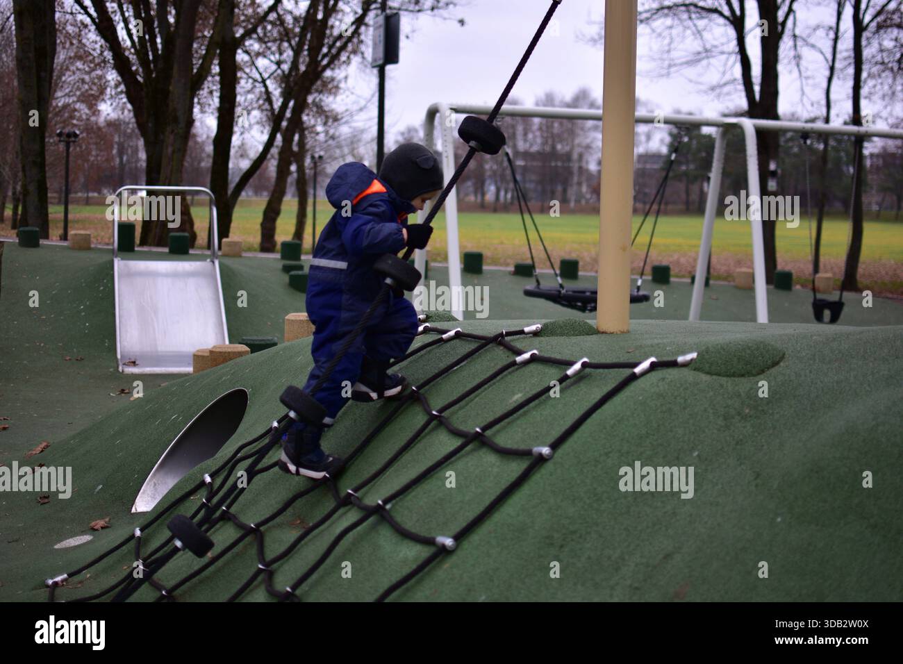Toddler climbing a rope net on a playground hill. Child develops ...