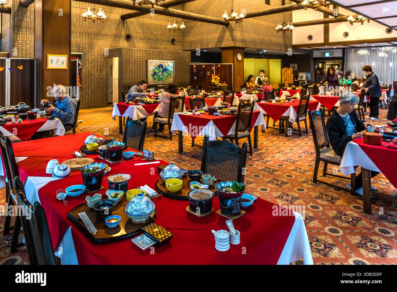 Guests eat breakfast in the wood-panelled dining room of the Watarase Onsen Hotel Sasayuri in the Hongu Valley. Traditional Japanese dishes are set out on red-covered tables. Hongucho Wataze, Tanabe, Wakayama Prefecture, Japan. Stock Photo