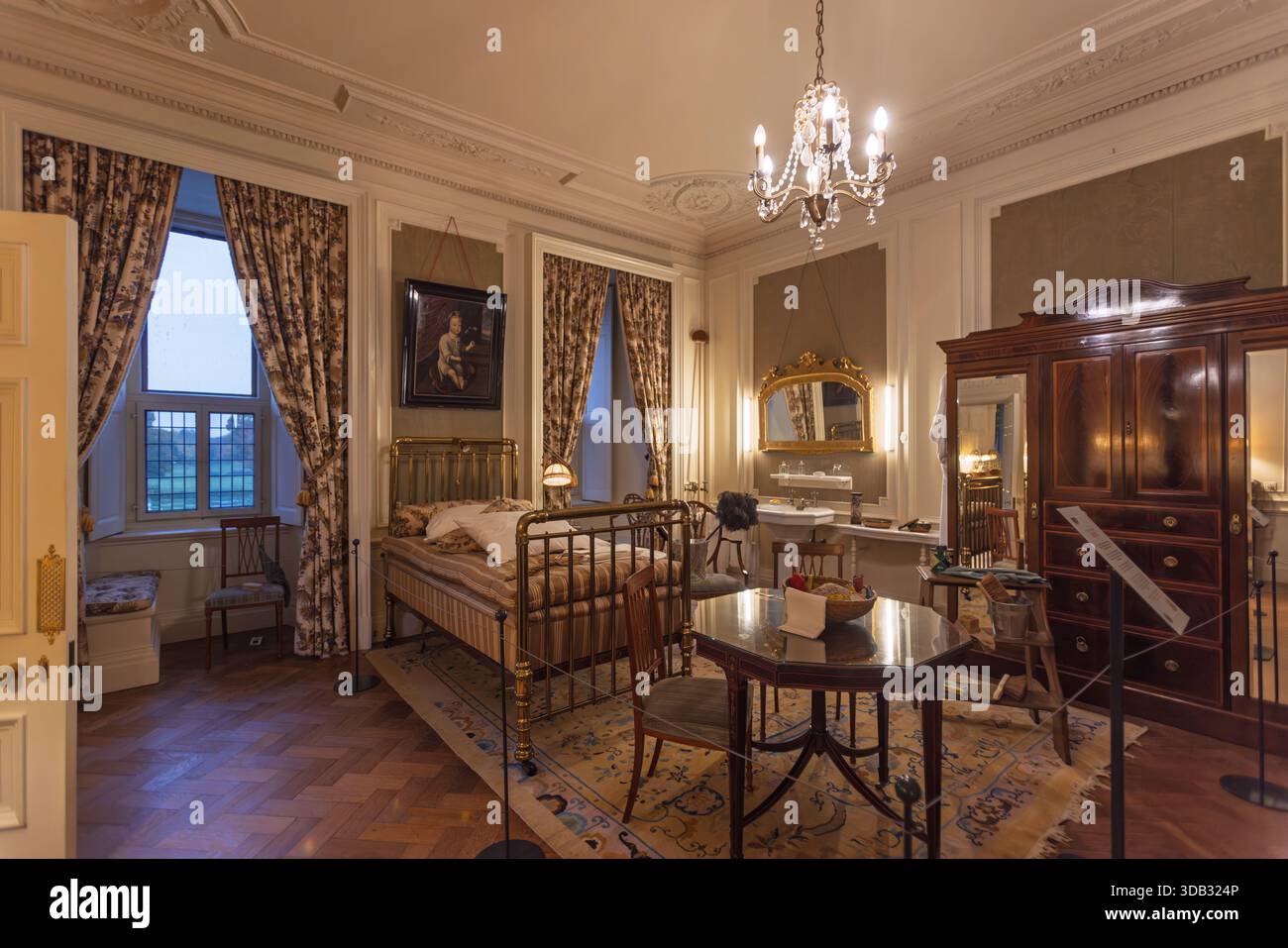 Elegant historic guest room inside Castle De Haar featuring a classic brass bed, antique wooden wardrobe, washbasin area, and ornate ceiling decoratio Stock Photo