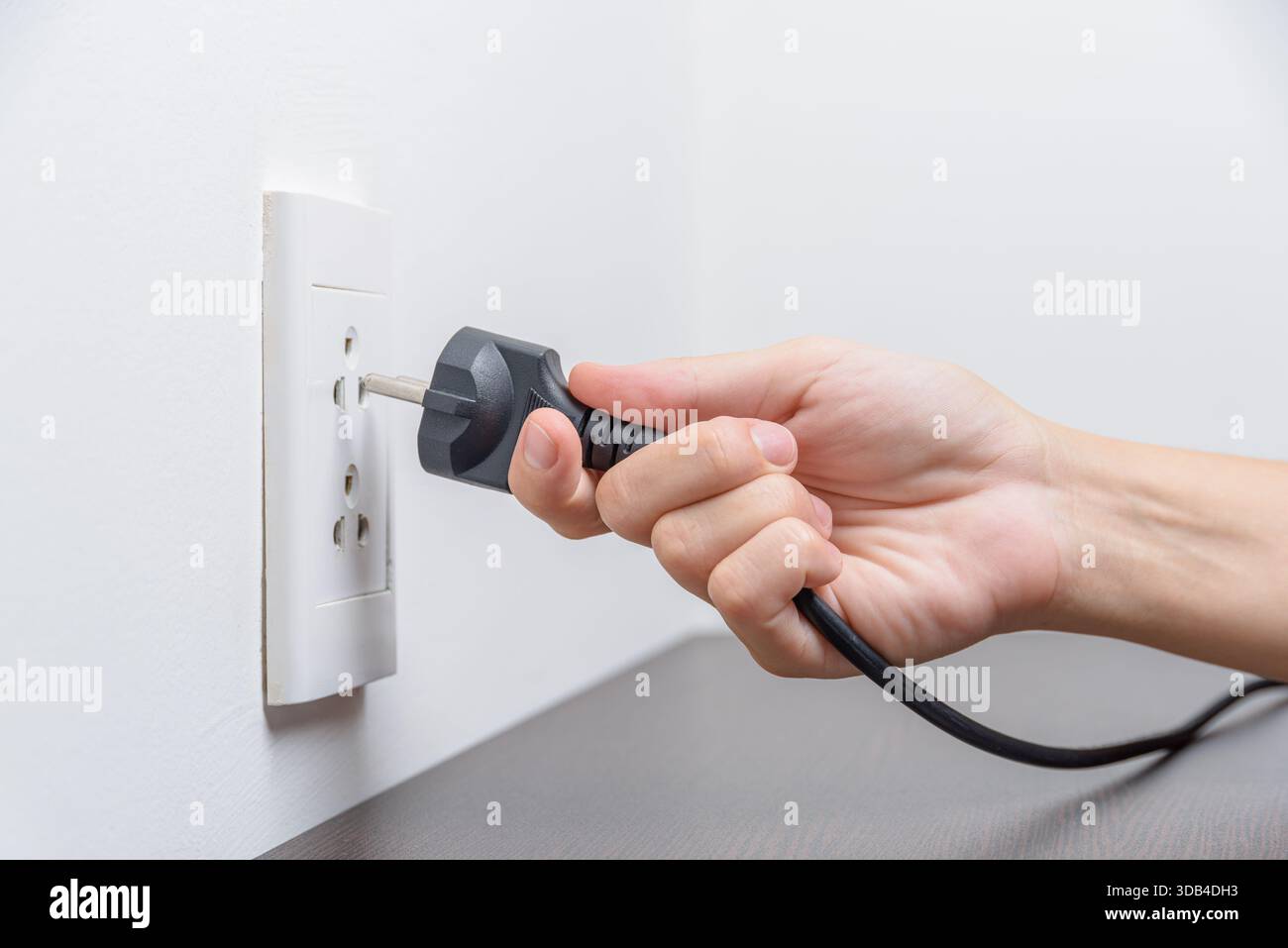 Female hand inserting a black electrical plug into outlet Stock Photo