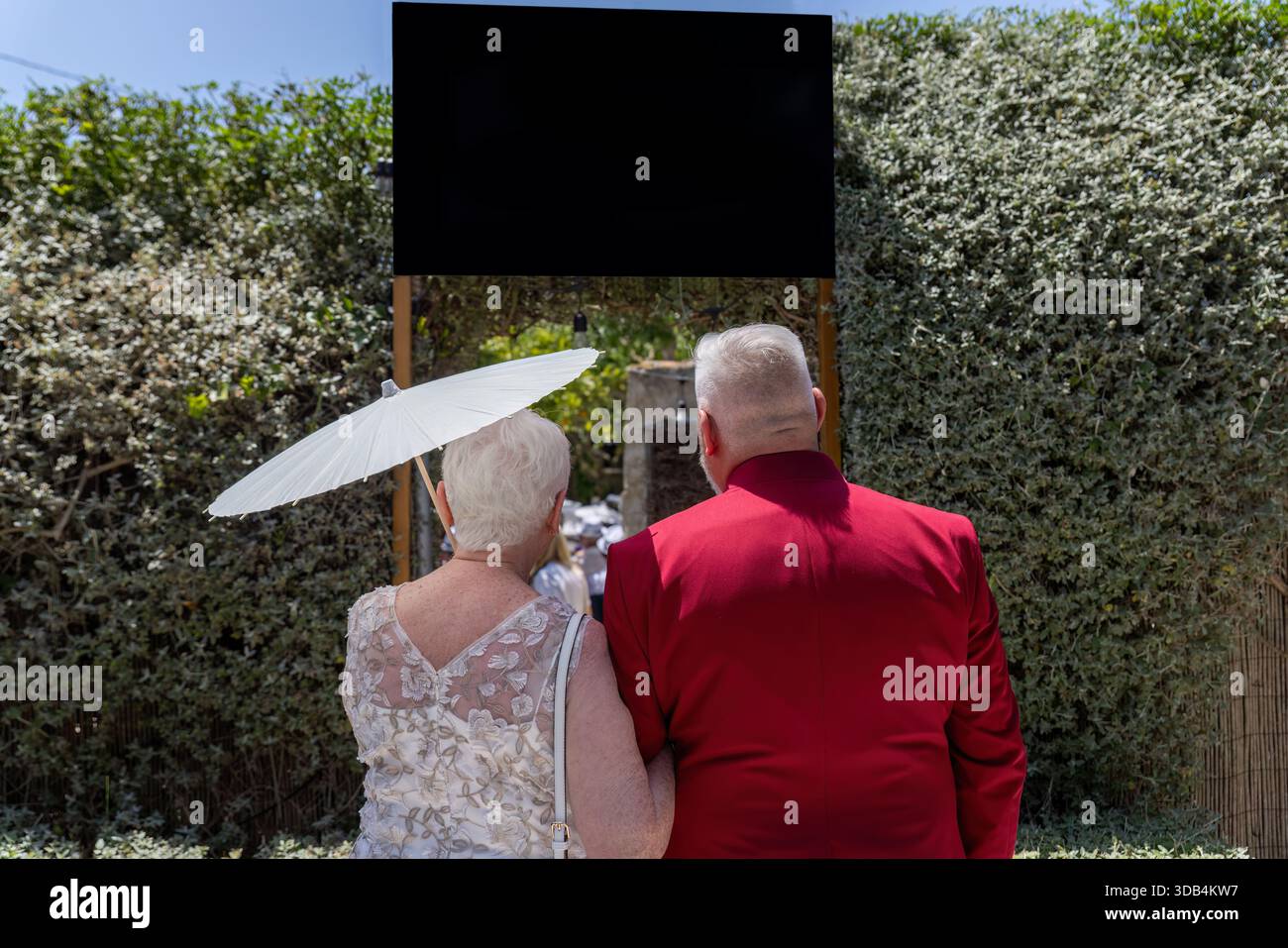 Senior couple facing wedding aisle, dressed formally with parasol on sunny  outdoor ceremony day Stock Photo - Alamy, image size:1300x957