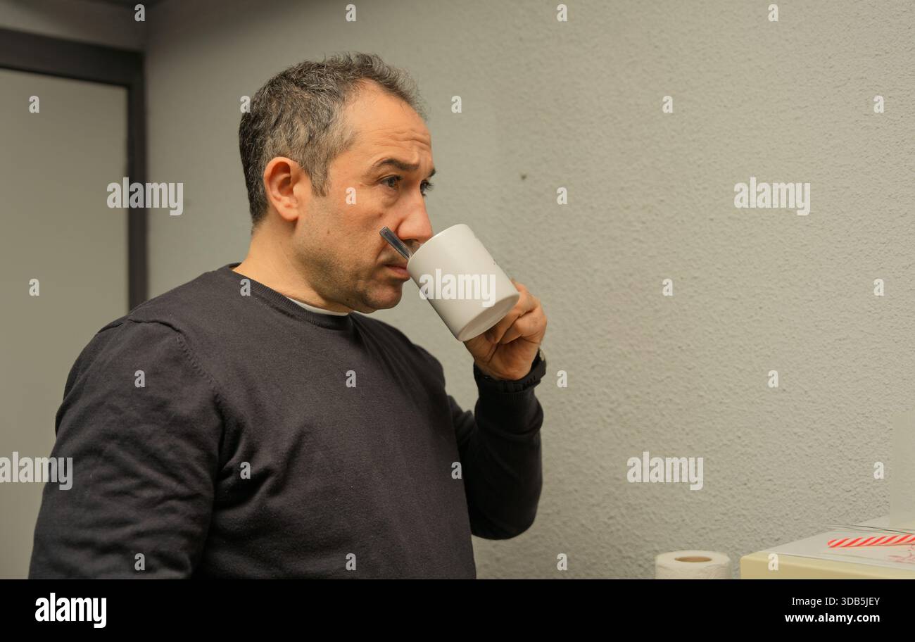 Man drinking from a white mug, pausing and thinking during a work break Stock Photo