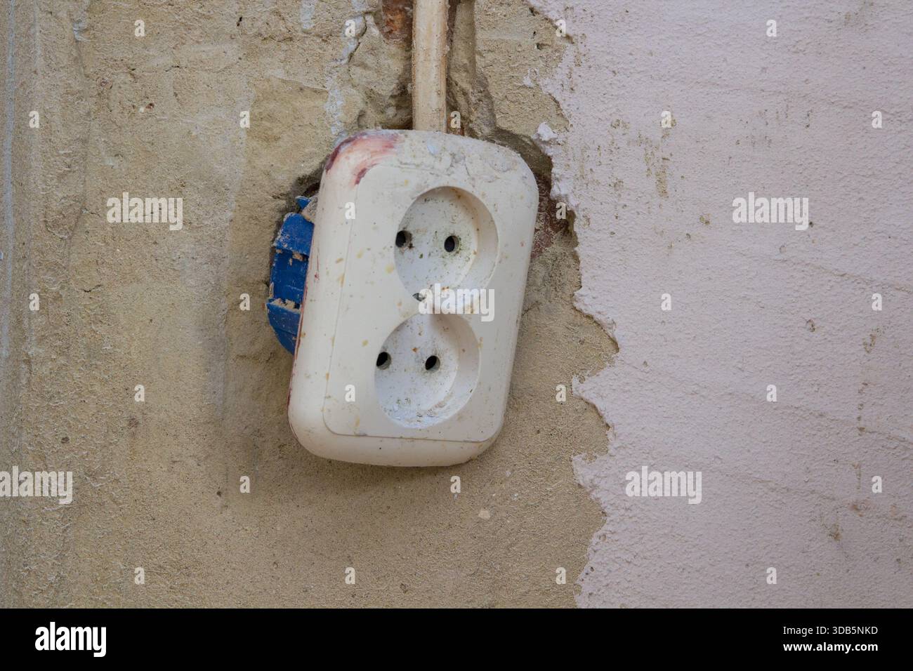 a white double socket hangs on the wall during repair Stock Photo