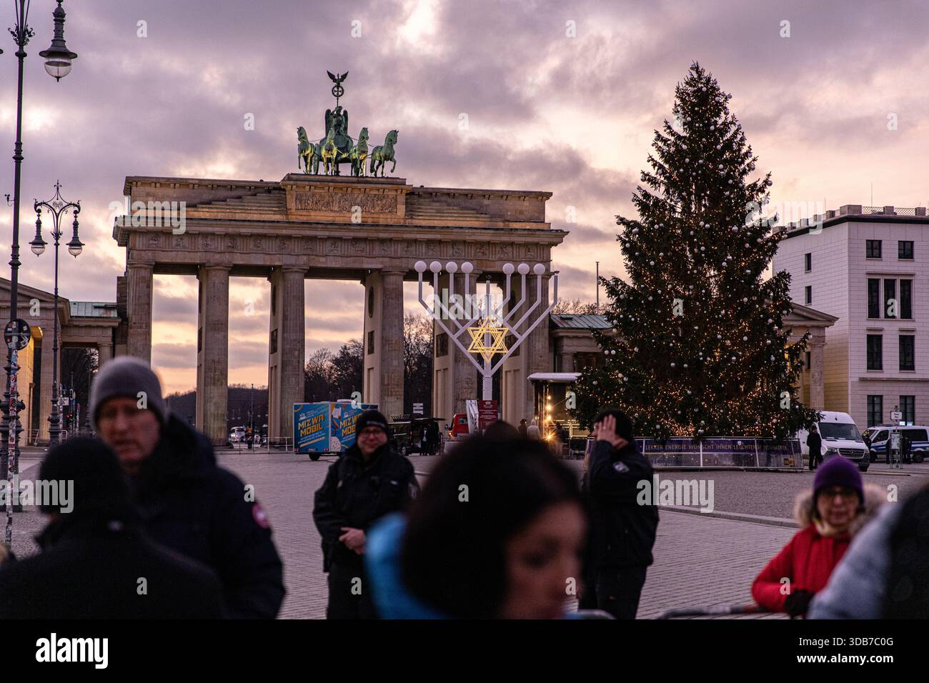 Berlin, Germany. 14th Dec, 2025. People walk past a large Hanukkah menorah  set up near the Brandenburg Gate as the sun sets in Berlin, Germany, on  Sunday, December 14, 2025. A Christmas