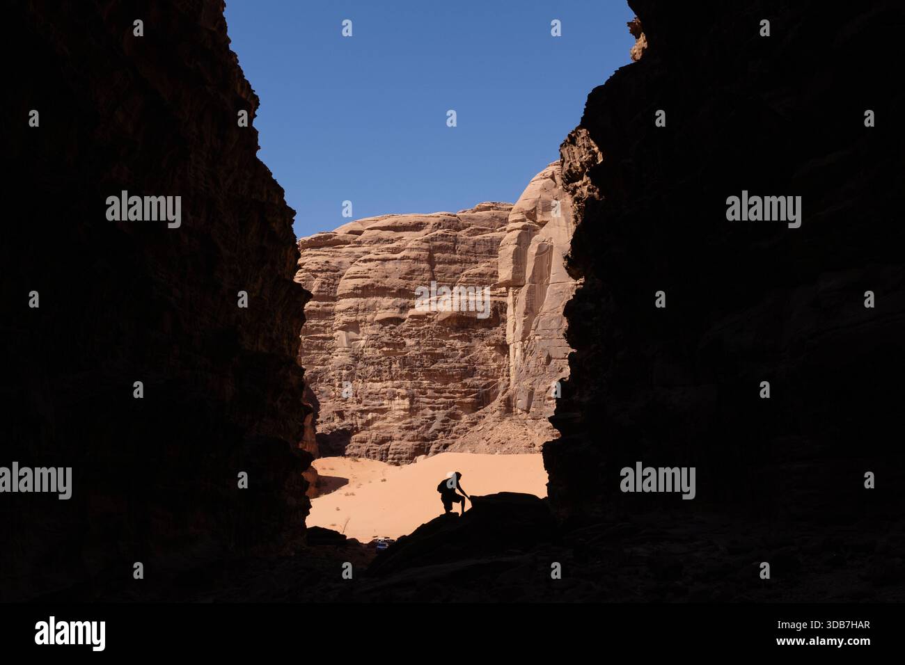 A person appears in silhouette inside a canyon in Wadi Rum, Jordan, surrounded by high sandstone walls and bright sunlight illuminating the rocks beyo Stock Photo