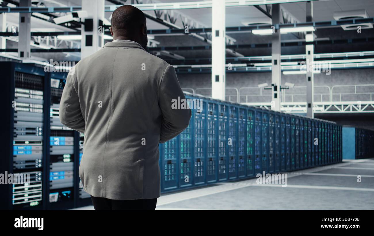 Admin walking in data center, doing inspection on infrastructure tech handling user requests. IT professional in server farm analyzing traffic patterns of equipment components, camera A Stock Photo