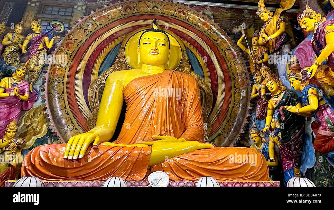 Colorful seated Buddha statue surrounded by disciples inside the Gangaramaya Temple in Colombo, Sri Lanka. - Stock Image
