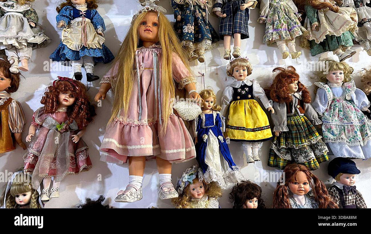 Group of vintage porcelain dolls hanging on a wall. - Stock Image