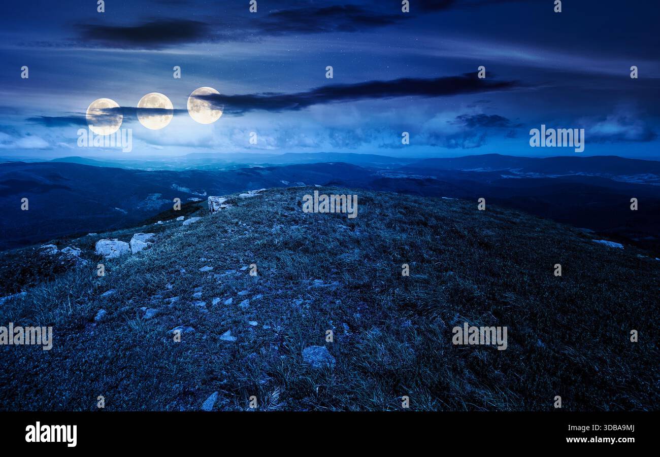 grassy slopes with boulders of mountain at night. beautiful summer scenery of alpine green environment under sky with clouds in full moon light. finan Stock Photo