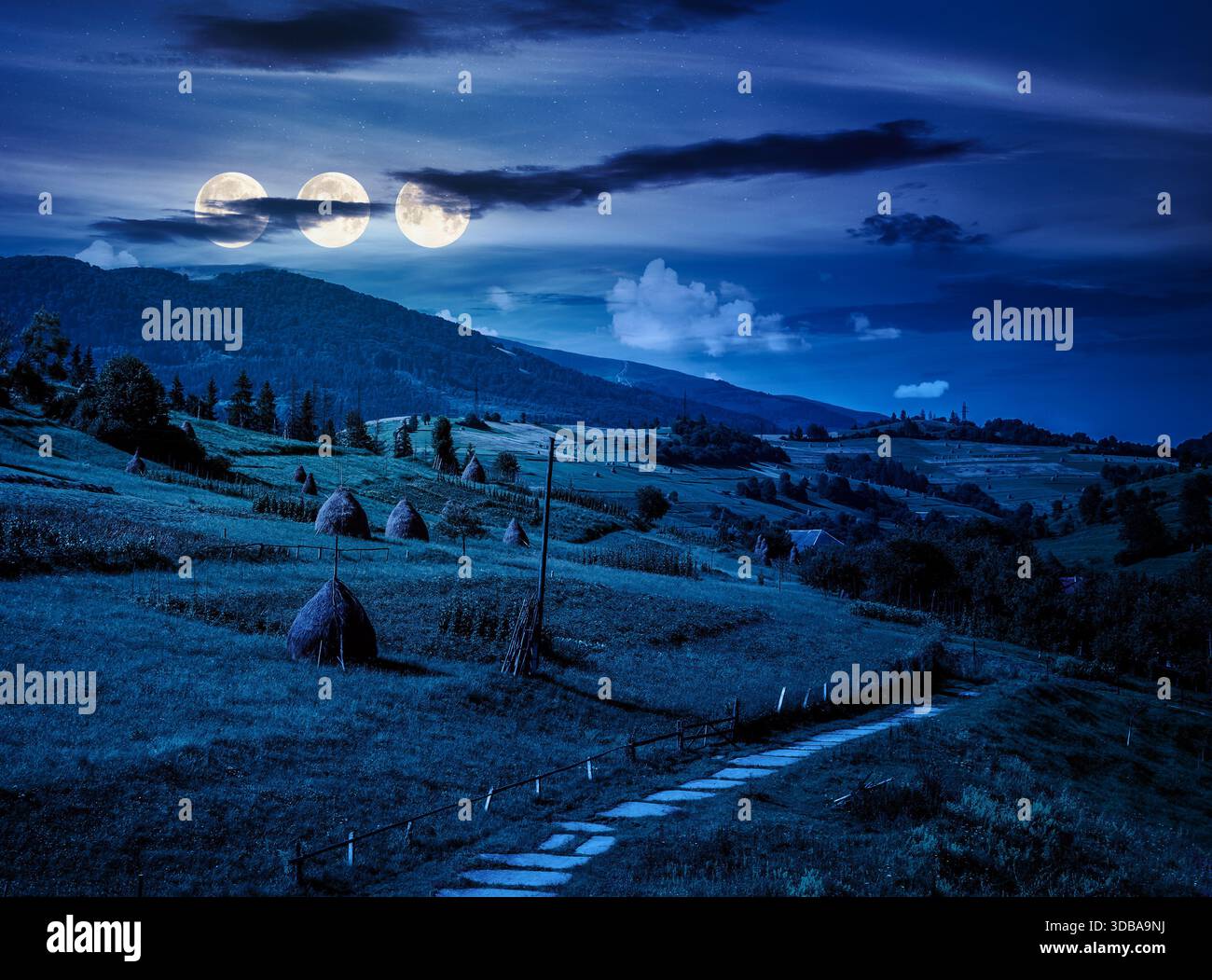 beautiful countryside scenery in summertime at night. haystack on grassy hillsides of mountain in full moon light. rolling landscape under cloudy sky. Stock Photo