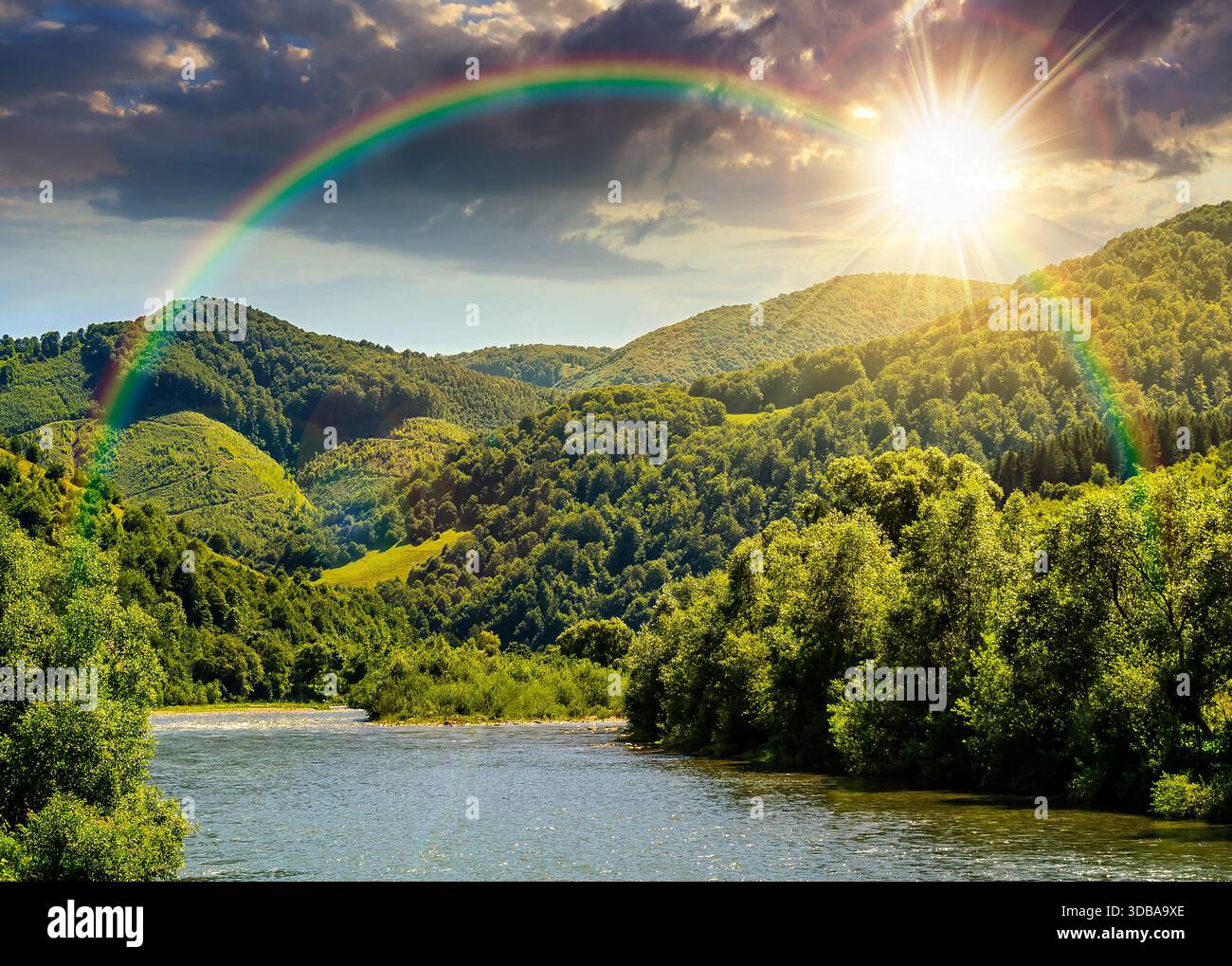river flows through green forest near mountain at sunset. picturesque nature of rural area on serene summer weather under clouds on sky in evening lig Stock Photo