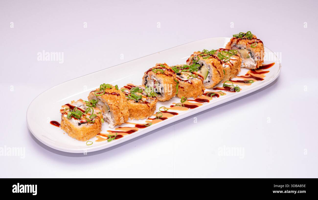 Deep fried sushi rolls with avocado, spring onions and sauce drizzle served on white ceramic plate isolated on white background. Stock Photo