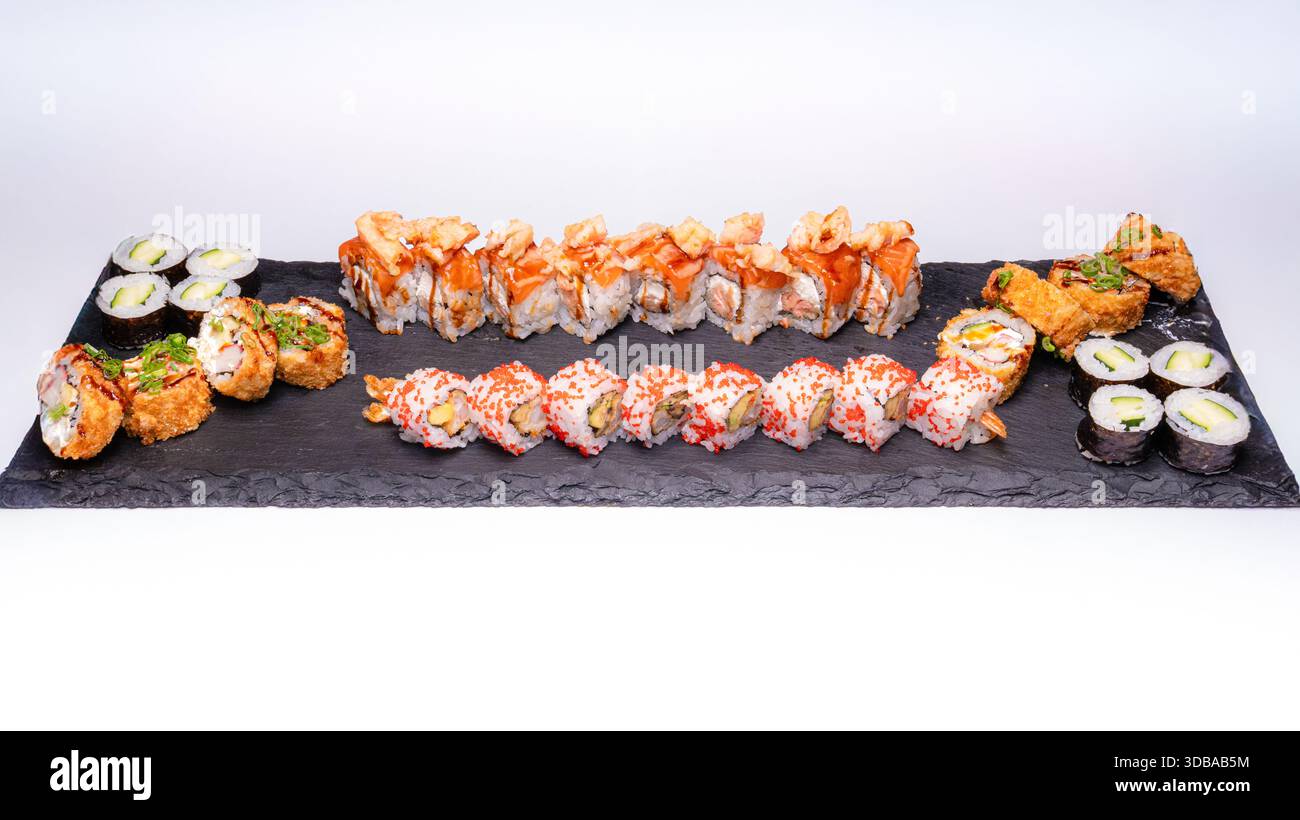 Assorted sushi platter with various sushi rolls and maki served on black slate board isolated on white background. Stock Photo