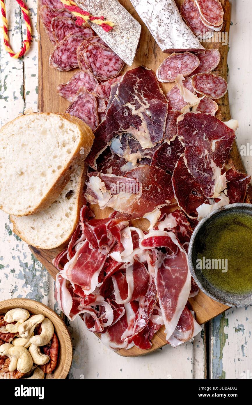 Snack board with traditional Spanish ham Jamon Iberico, sliced Fuet sausage, green olives, white bread, nuts, olive oil. Light rustic wooden backgroun Stock Photo